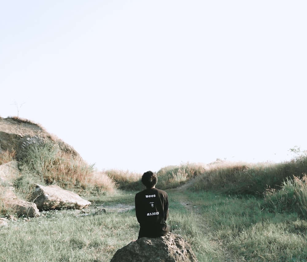 man in black jacket sitting on rock during daytime