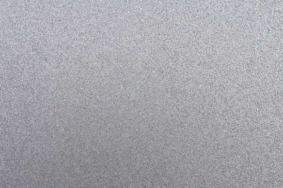 A textured surface with numerous small, grainy particles creating a uniform pattern. The surface appears metallic or granular, composed mainly of various shades of gray.