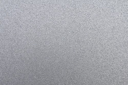 A textured surface with numerous small, grainy particles creating a uniform pattern. The surface appears metallic or granular, composed mainly of various shades of gray.