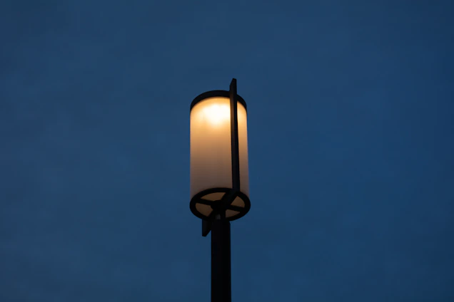 A sleek, modern LED streetlight glowing softly against a twilight cityscape with subtle schematic line-art overlay.