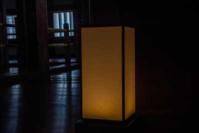 Side view of the Lamela #001 lamp on a wooden table with warm light casting gentle shadows on a white wall.