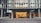 The entrance of a modern office building displays the large 'wework' logo above its door. The structure features a glass facade with a visible interior showing desks and office furniture. The exterior includes metal framework that adds to the contemporary aesthetic.