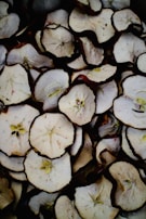 A close-up view of multiple slices of dried apples arranged in a pile. The slices show both the flesh and the seeds, with the brown edges indicating their dried nature.