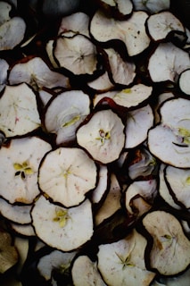A close-up view of multiple slices of dried apples arranged in a pile. The slices show both the flesh and the seeds, with the brown edges indicating their dried nature.