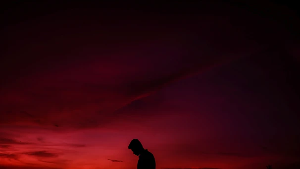 A dramatic still from a cinematic short film featuring a silhouette against a glowing red sunset.