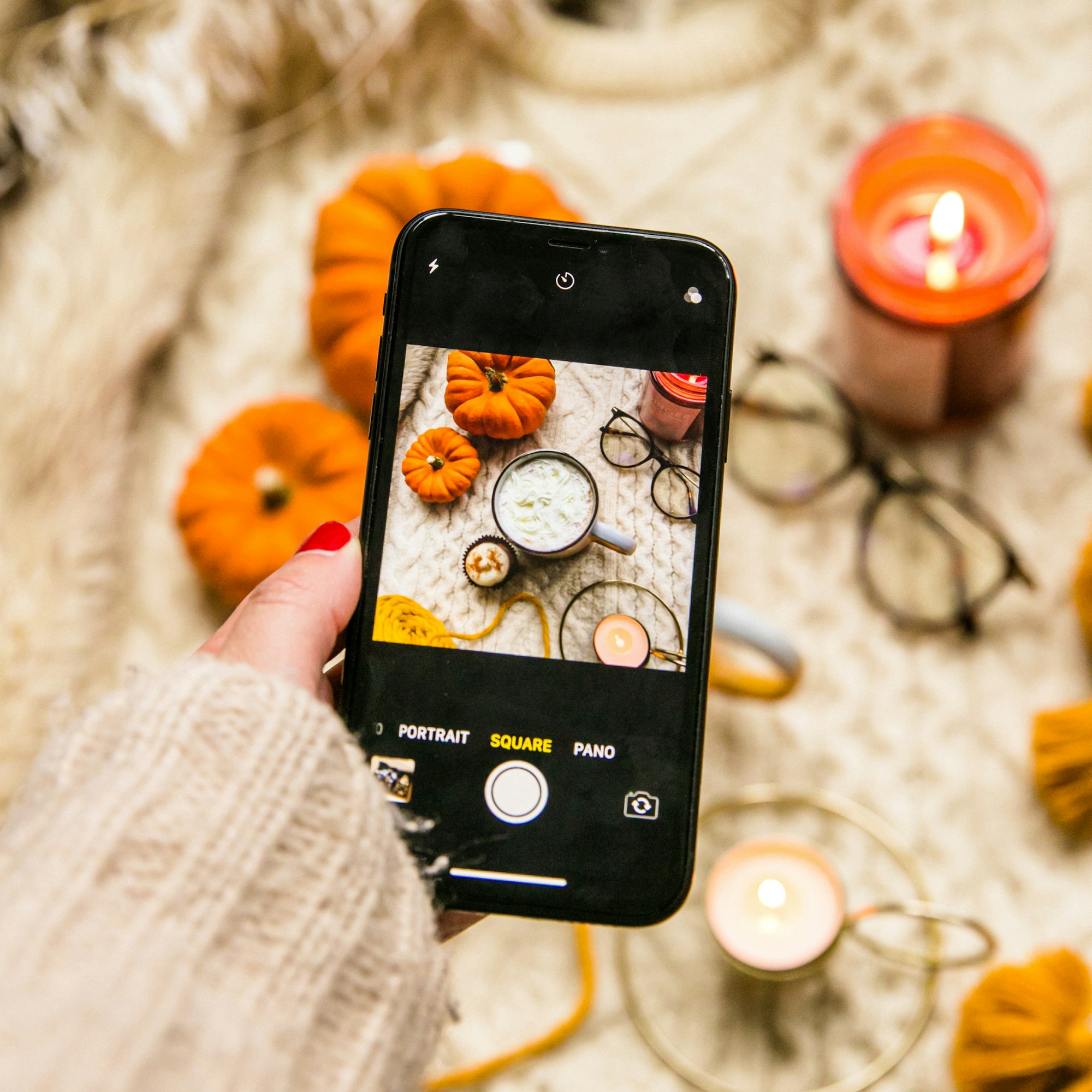 Smartphone taking photo of Halloween business decorations like pumpkin, candles, and autumn colorings.