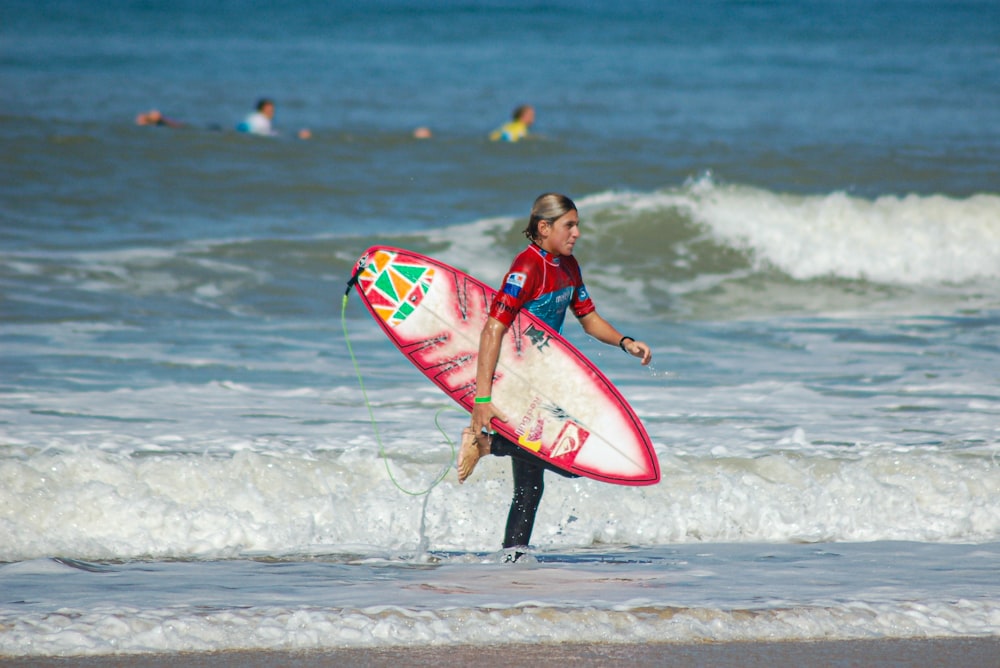 girl in red and black wet suit holding red and white surfboard on beach during daytime