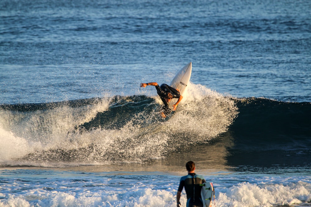 man in black wet suit holding white surfboard on sea waves during daytime