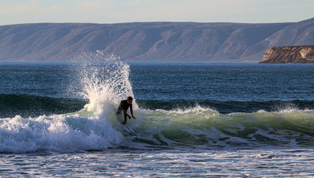 man in black wet suit surfing on sea waves during daytime