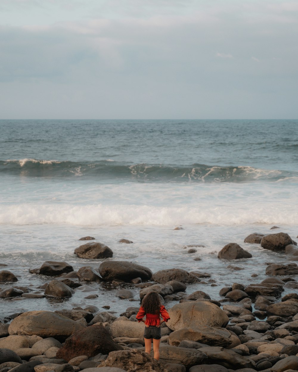 Persona con sudadera con capucha roja sentada en la orilla rocosa durante el día