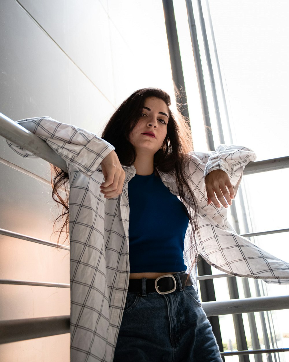 woman in blue shirt and white jacket standing beside glass window