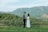 Happy young couple standing in front of their new land plot with green fields behind them.