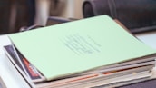A stack of financial books and a notebook with handwritten notes on a wooden desk.