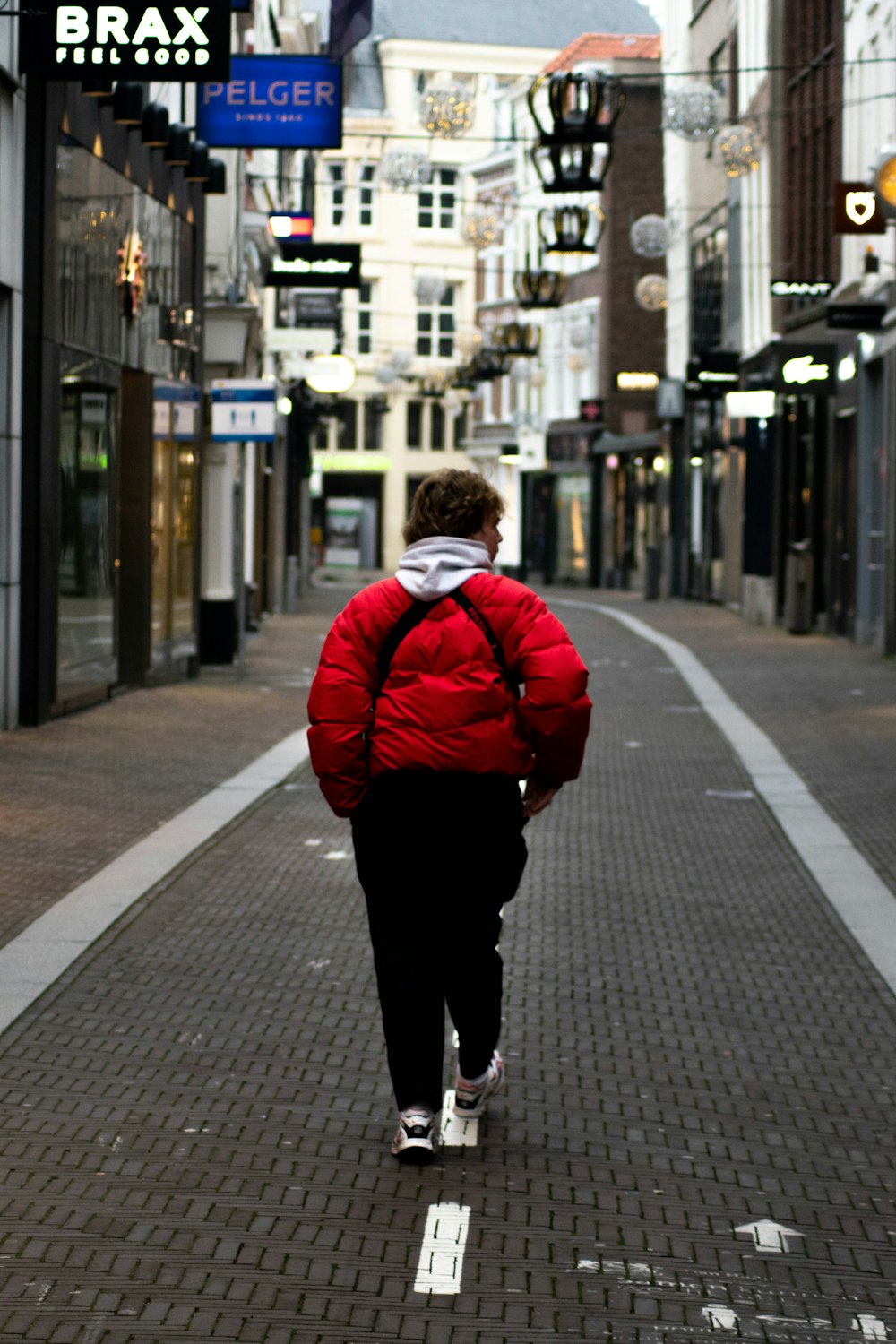 man in red jacket walking on sidewalk during daytime