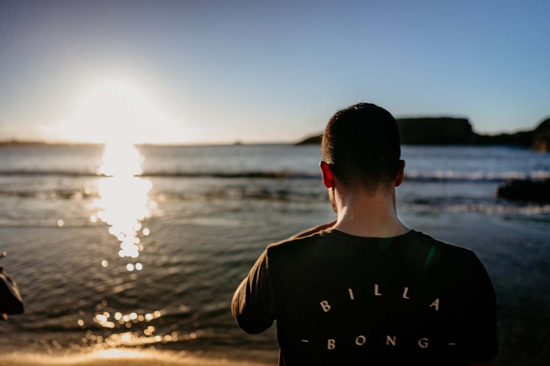 man in black crew neck t-shirt standing on seashore during sunset