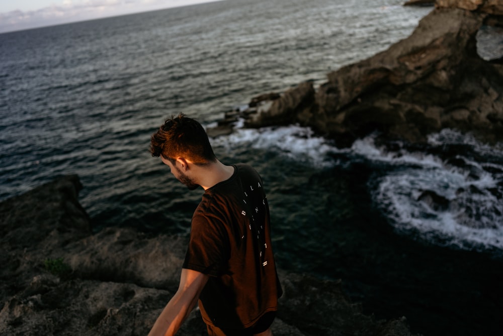 man in brown crew neck t-shirt standing on rocky shore during daytime