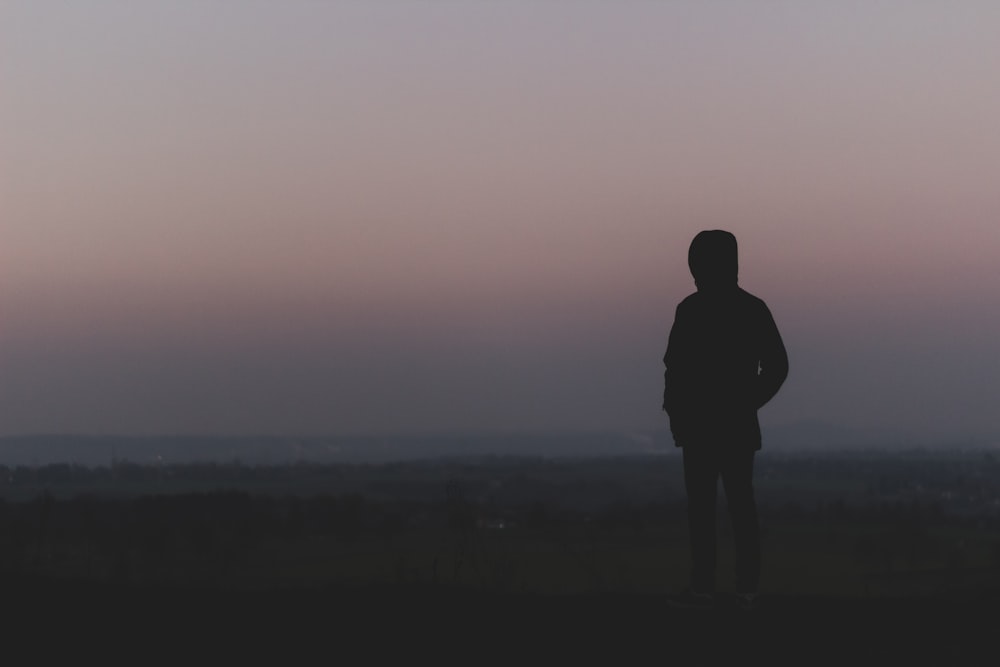 silhouette of man standing on hill during sunset