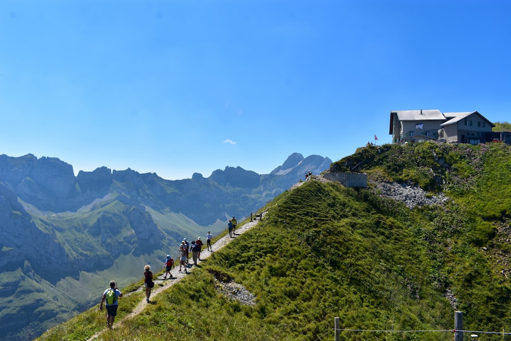 Menschen, die tagsüber auf einem grünen Grasfeld in der Nähe des Berges unter blauem Himmel spazieren gehen