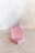 Two bars of pink soap, with one bar leaning against the other on a textured, light-colored surface. The soap has a smooth appearance with small specks, possibly of natural ingredients, and a rough edge on top.