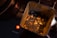 The image shows a tin container filled with loose leaf tea, which appears to be a blend containing pieces of dried fruit or spices. It is placed on a stovetop, indicated by the glowing red light and the words 'HOT SURFACE' printed nearby.
