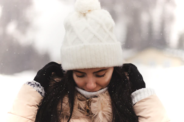 Outdoor scene with a person wearing a woolora hat, snow gently falling around them.