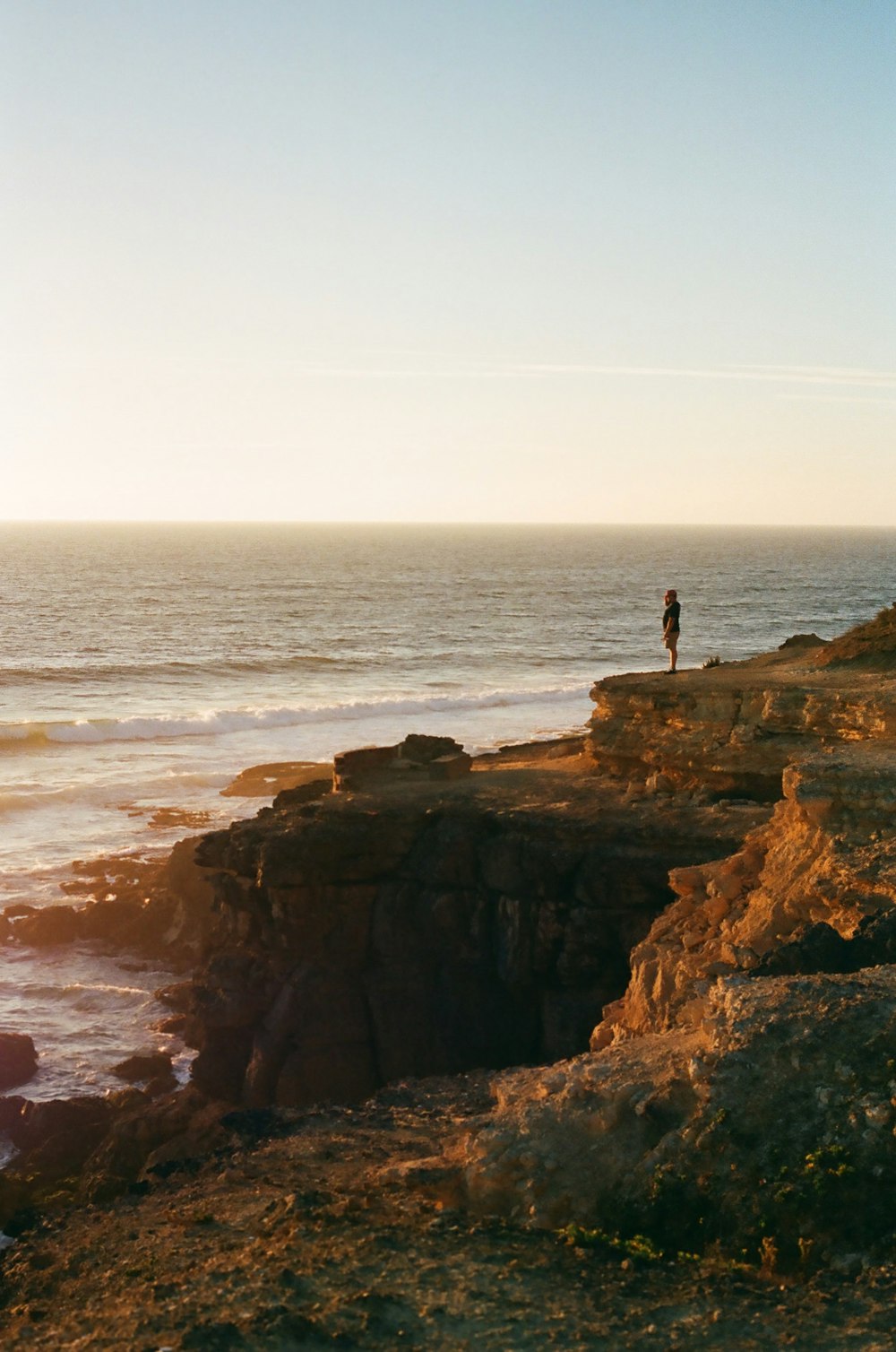 Person, die tagsüber auf einer Felsformation in der Nähe des Meeres steht