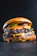 Close-up of a juicy smoked burger with melted cheese and fresh pickles on a dark rustic background.