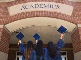 three girls in graduation gowns hold their caps in the air