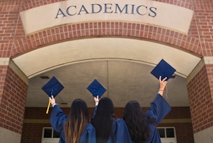 three girls in graduation gowns hold their caps in the air