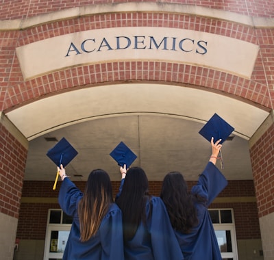 three girls in graduation gowns hold their caps in the air