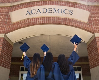 three girls in graduation gowns hold their caps in the air