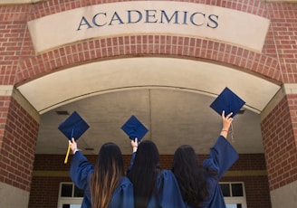 three girls in graduation gowns hold their caps in the air