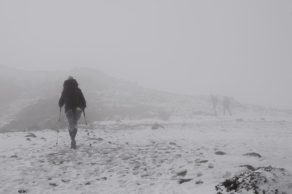 donna in giacca nera che cammina sul campo coperto di neve durante il giorno