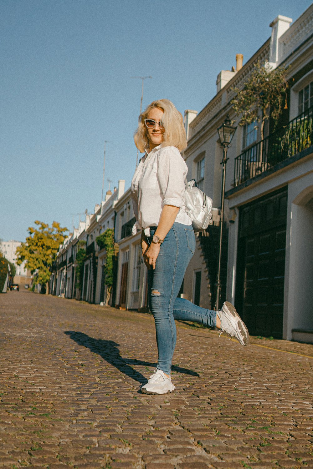 Mujer con camisa blanca y jeans de mezclilla azul de pie sobre piso de concreto marrón durante el día