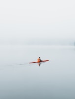 A kayaker navigating through mist rising from a still lake in early morning.