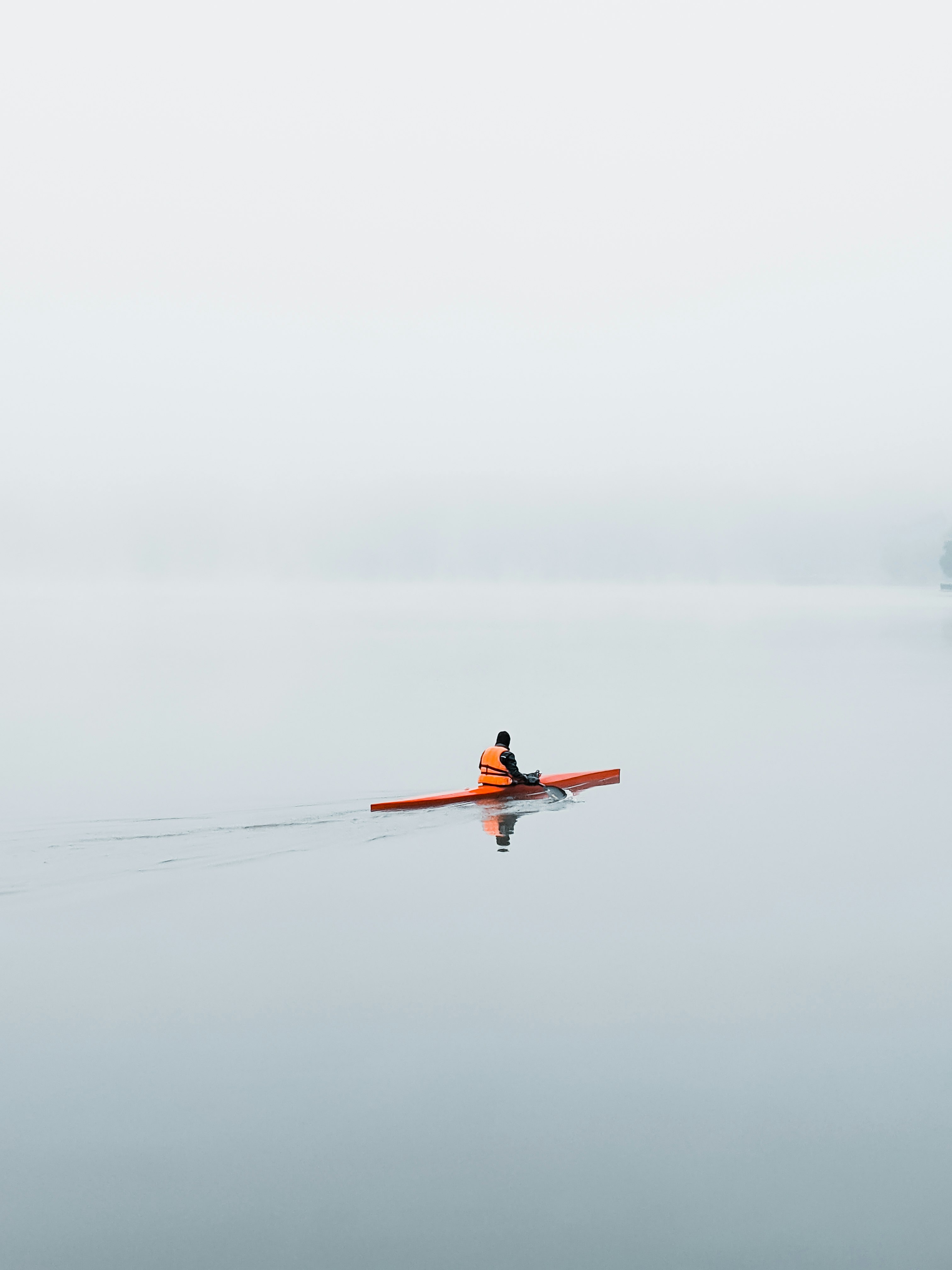 person in red jacket and black pants riding orange kayak on body of water during daytime