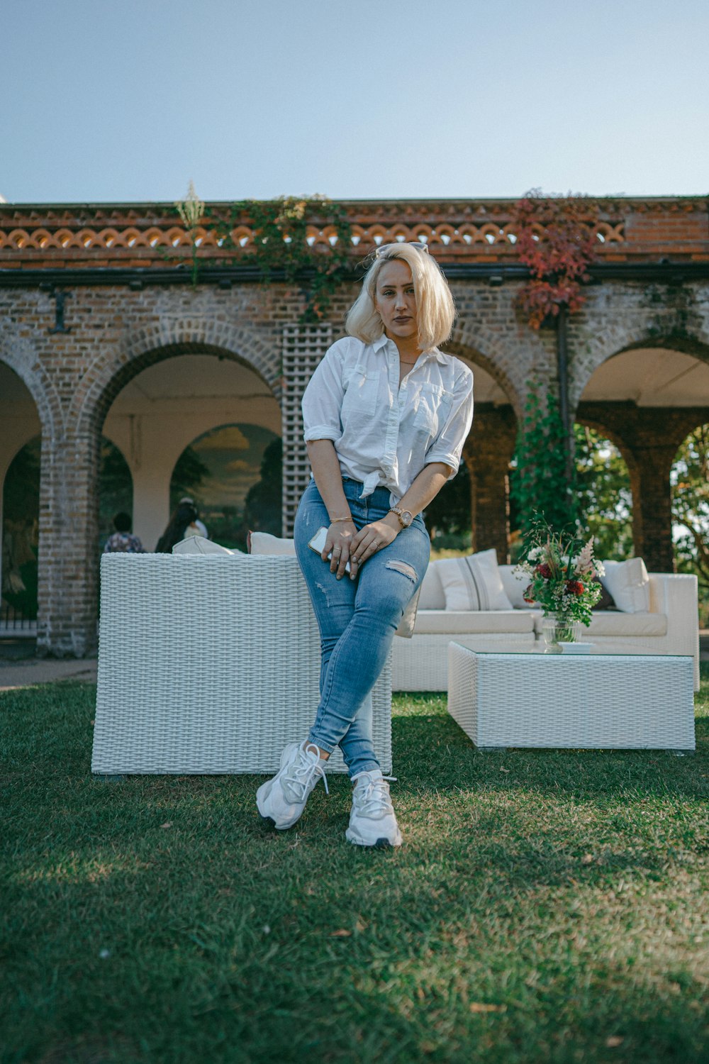 woman in white dress shirt and blue denim jeans standing on green grass field during daytime