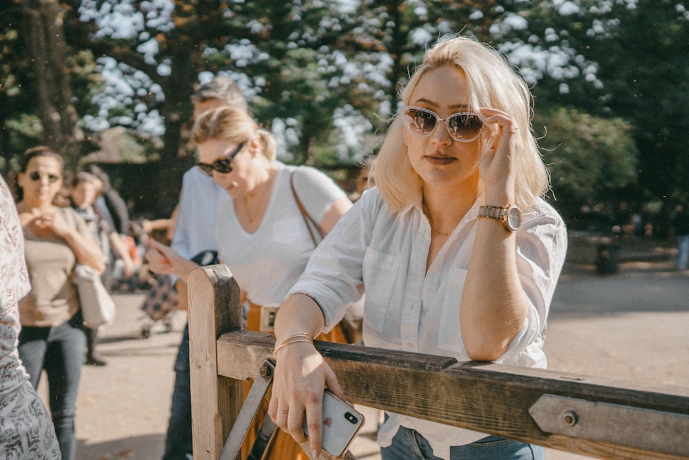 Frau im weißen Langarmhemd mit Sonnenbrille sitzt auf der Bank