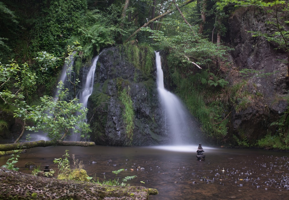 person in black jacket sitting on rock in front of waterfalls during daytime