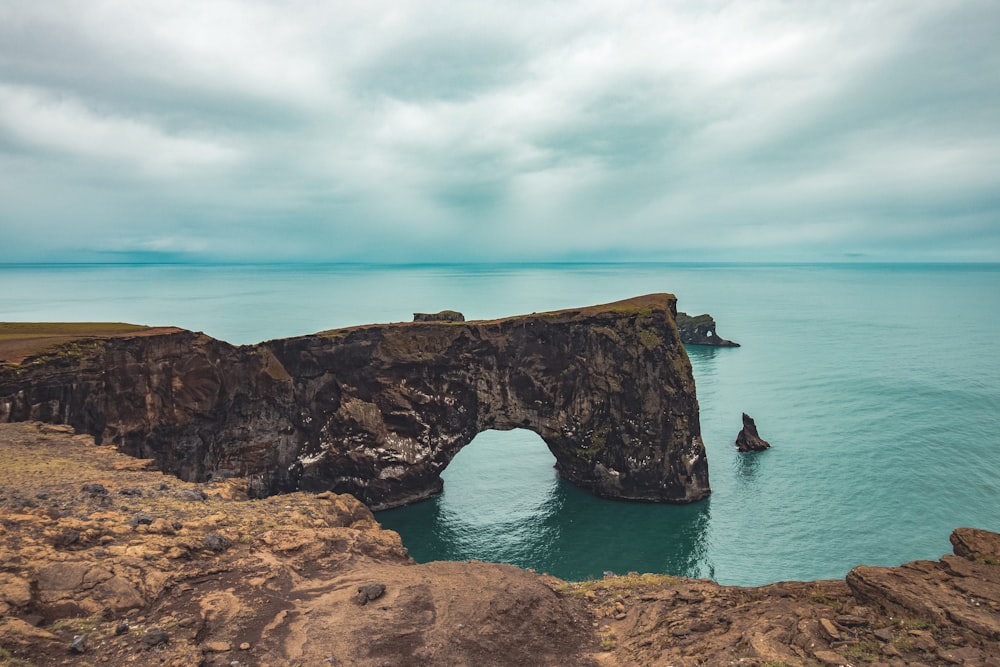 brown rock formation on sea under gray clouds