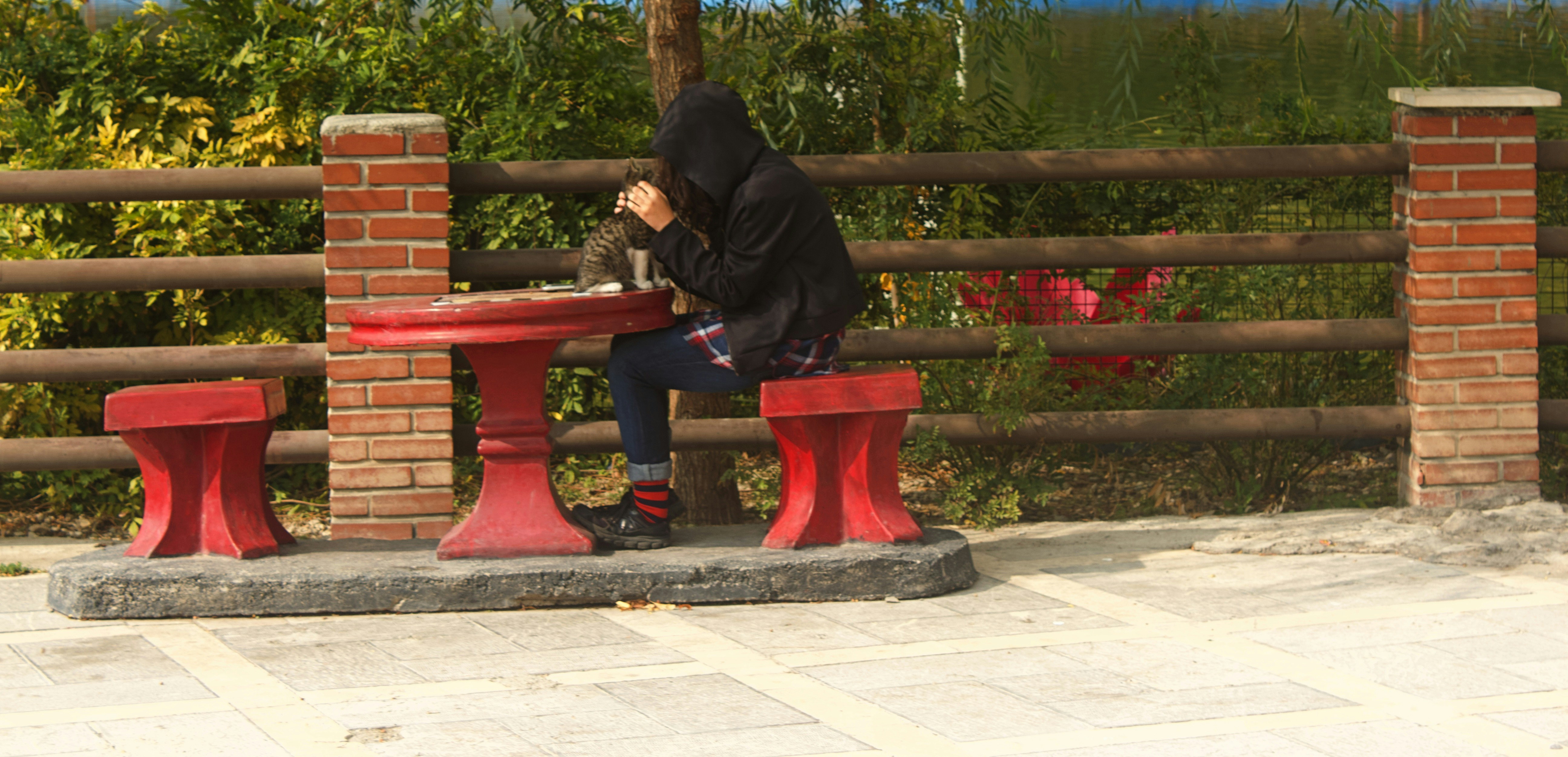 man in black jacket sitting on red wooden bench