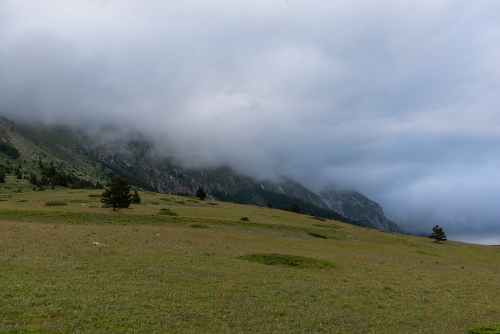 green grass field near mountain under white clouds during daytime