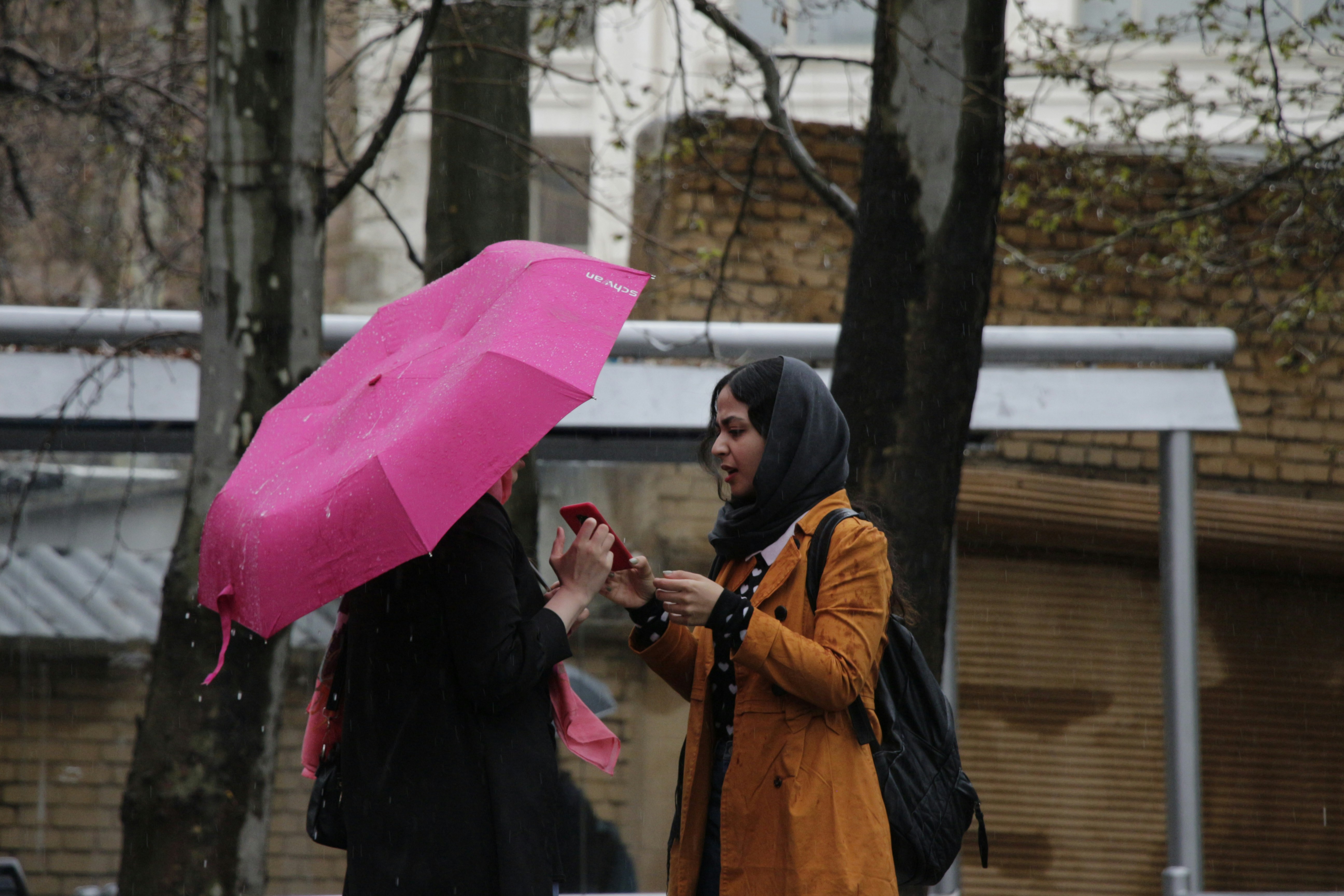 2 women in black and orange coat holding pink umbrella