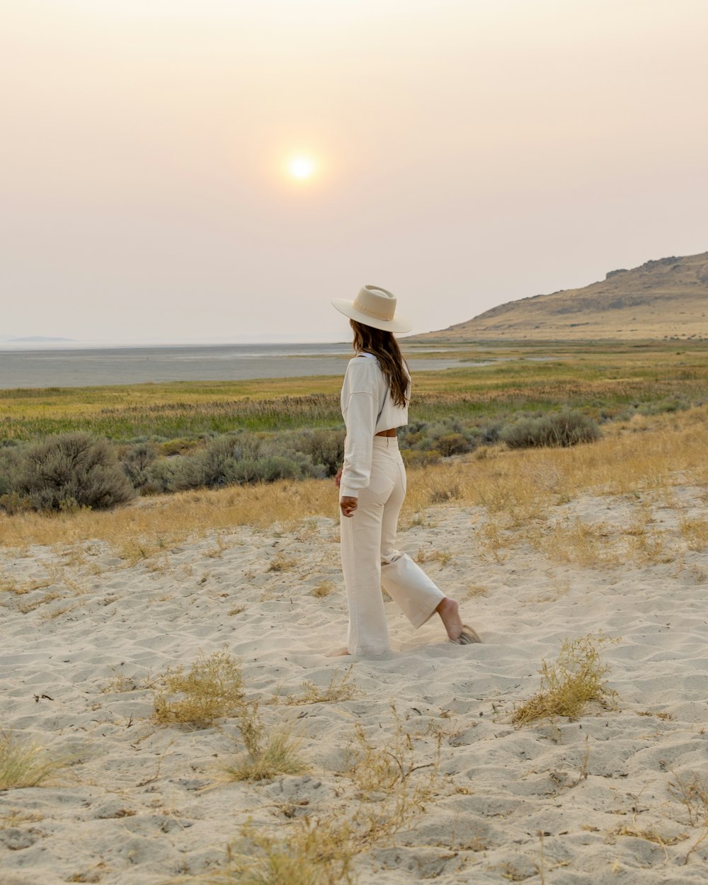 femme en robe blanche debout sur le champ brun pendant la journée