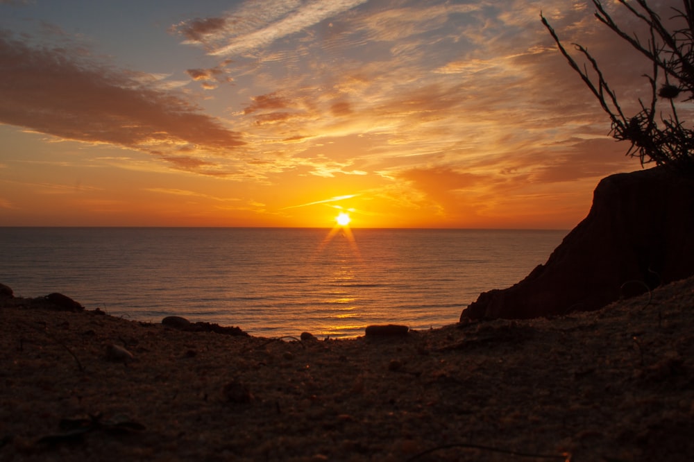 silhueta da pessoa em pé na rocha perto do mar durante o pôr do sol