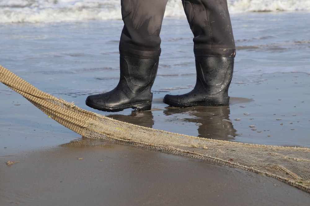 person in black leather boots standing on brown wooden dock during daytime