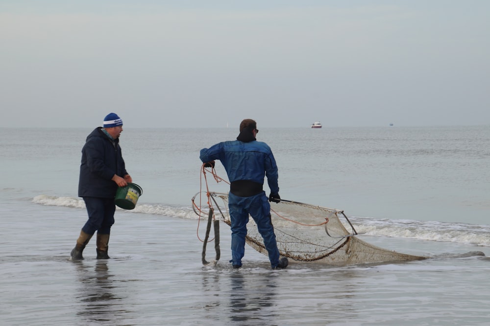 man in blue jacket and black pants holding brown wooden stick on body of water during