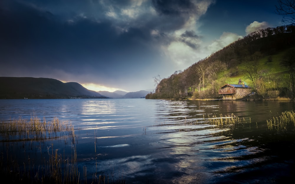 brown wooden house near lake and mountain under blue sky during daytime