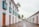 A picturesque cobblestone street lined with historic white colonial-style buildings adorned with vibrant doors and windows. The architecture features turquoise accents and wooden shutters. Tall palm trees punctuate the scene, adding a tropical touch to the serene environment.