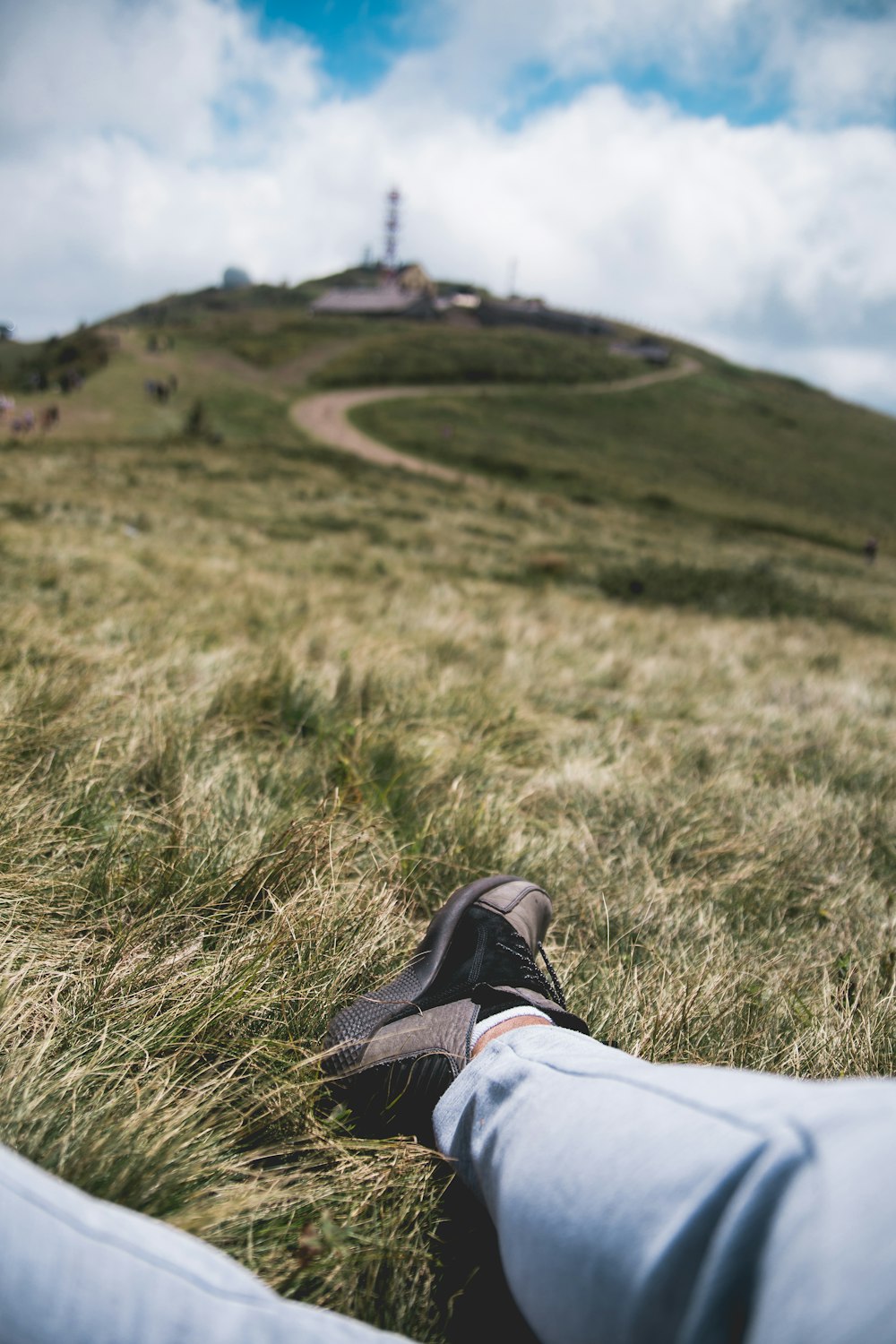 person in white pants and brown hiking shoes sitting on grass field during daytime